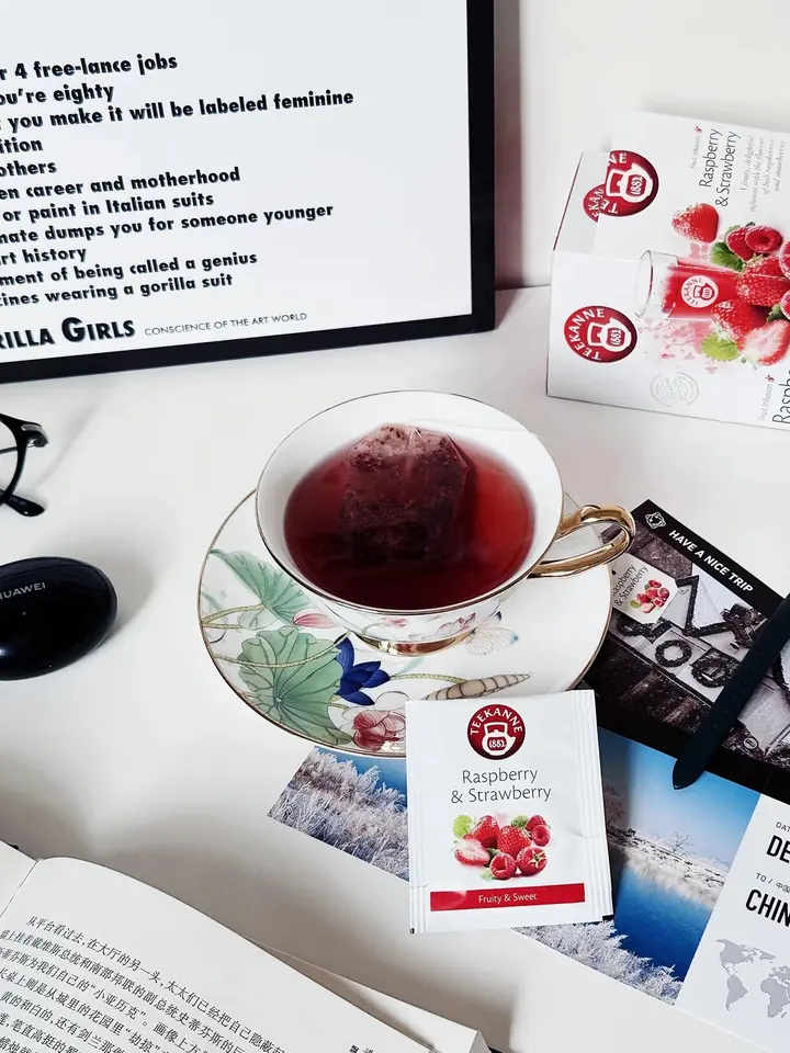Consumer photo of TEEKANNE Raspberry & Strawberry tea served in a cup with sachet and box visible.