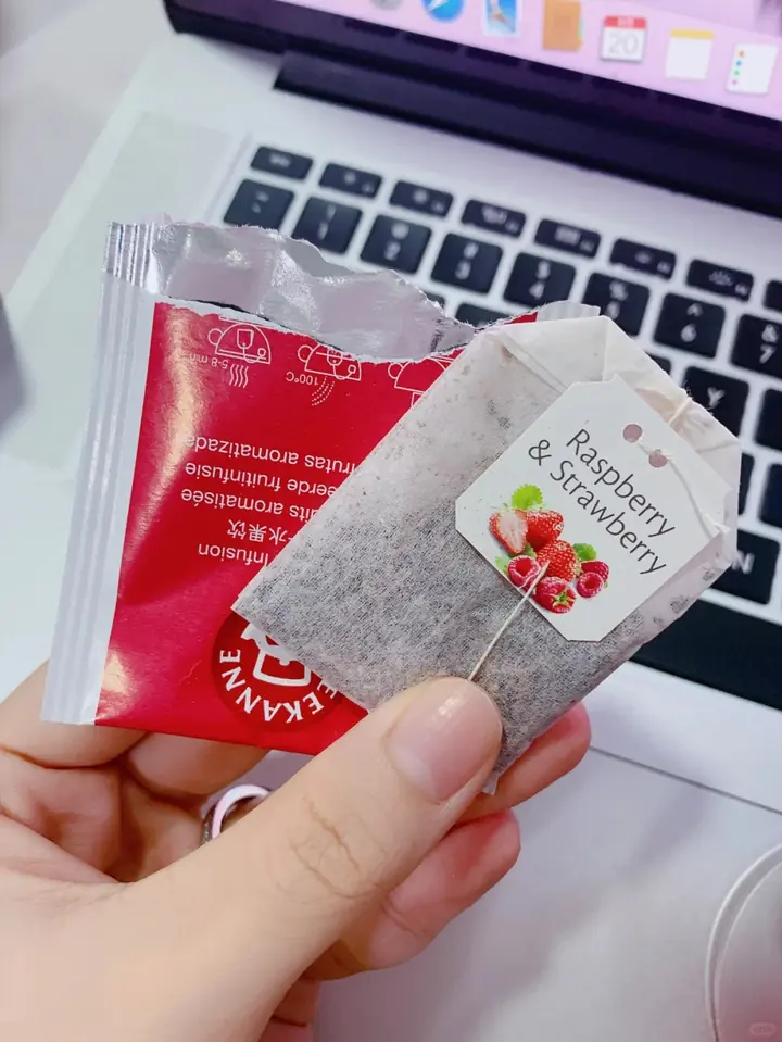 Consumer photo of a TEEKANNE Raspberry & Strawberry tea bag opened near a laptop keyboard.