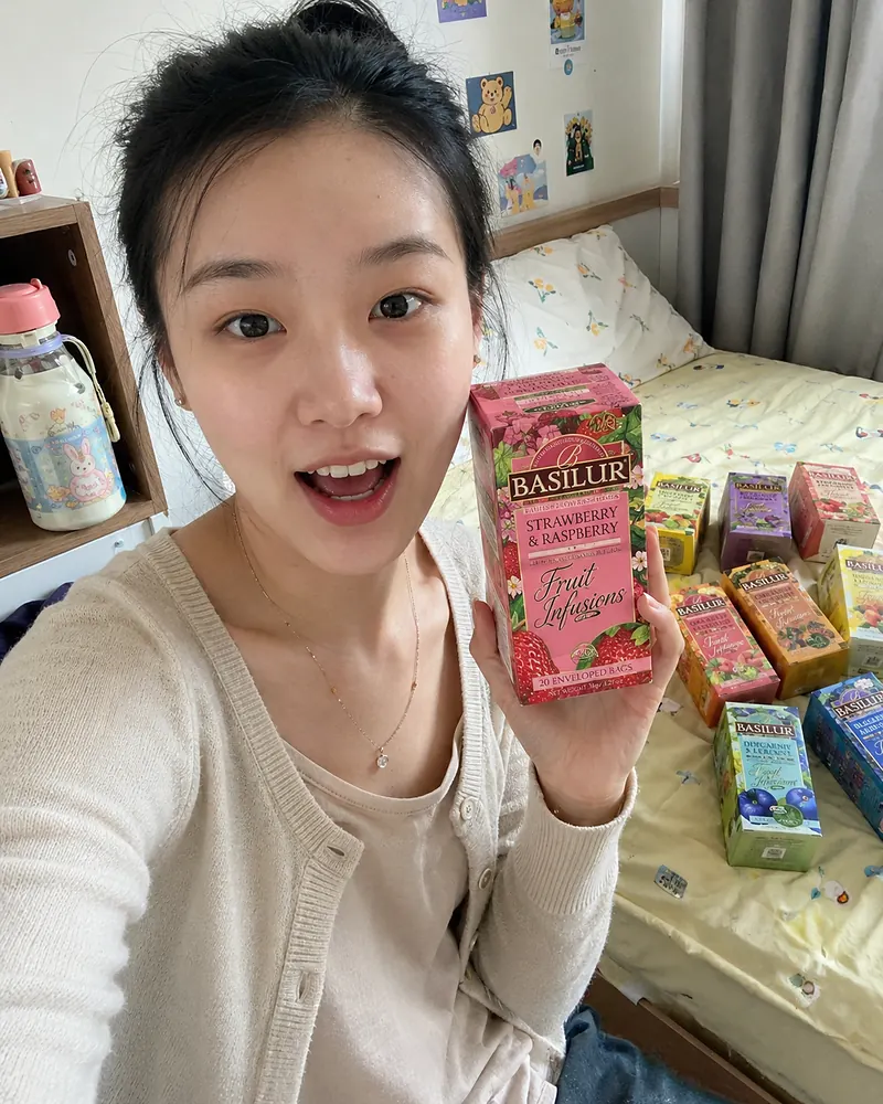 A young woman holding a fruit infusion box with multiple flavour boxes arranged on a bed.