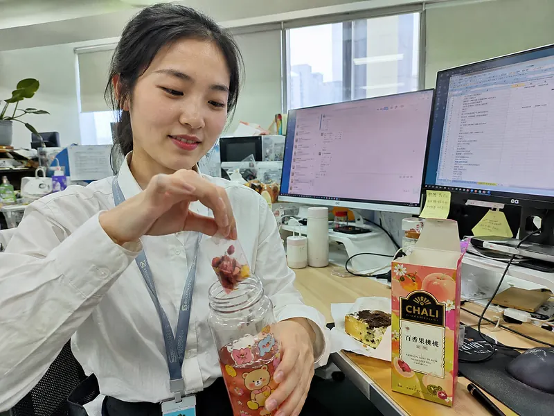 A young office worker preparing a fruit tea infusion in a bottle at her desk.